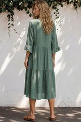 Woman wearing a green dress standing against a white wall with greenery.