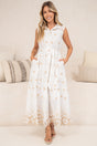 A smiling woman wearing the Bruna Midi Dress in Palmira Print, a white sleeveless collared button-front shirt dress with peach embroidered florals, tie waist and embroidered hem, styled with tan sandals in front of a cream sofa with neutral cushions