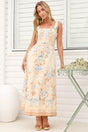 A woman wearing the Camelia midi dress in a dusty blue and tan floral print, featuring a square neckline and wide straps, standing in front of a white panelled wall.