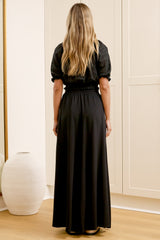 Wearing high-waisted black pants with a gathered paper-bag waist and wide-leg fit, a woman stands in front of a warm beige closet.
