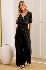 Wearing high-waisted black pants with a gathered paper-bag waist and wide-leg fit, a woman stands in front of a warm beige closet.