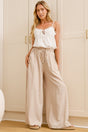 A woman wearing sand-coloured wide-leg pants with a high elasticated waist and relaxed fit, standing in front of a warm beige closet.
