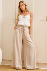 A woman wearing sand-coloured wide-leg pants with a high elasticated waist and relaxed fit, standing in front of a warm beige closet.