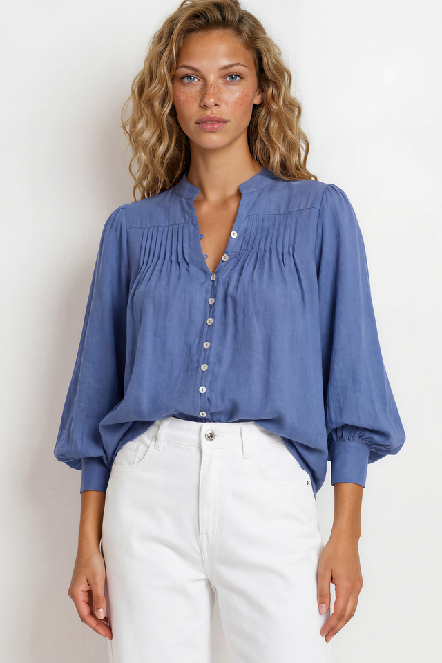 Woman wearing a blue blouse and white pants against a plain background