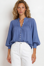 Woman wearing a blue blouse and white pants against a plain background