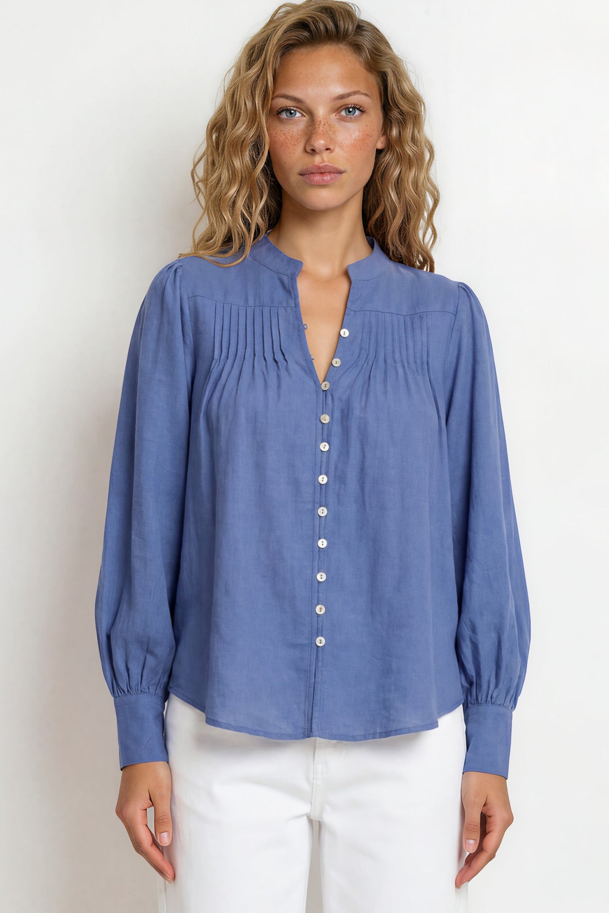 Woman wearing a blue blouse with white pants against a plain background