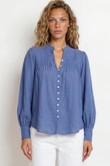 Woman wearing a blue blouse with white pants against a plain background