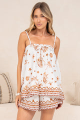 A woman wearing the Clea Top in Andros Print, a white ruffle hem cami with a rust tiger and palm print, styled with the matching Chios Shorts against a soft beige backdrop