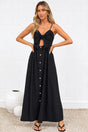 A woman modeling a black midi dress with spaghetti straps, a keyhole cutout at the bust, and a button-down front, standing in a minimalist room with a white brick wall and light-colored rug.