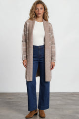 Woman wearing a long beige cardigan, white top, blue jeans, and brown shoes on a white background