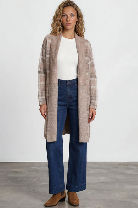Woman wearing a long beige cardigan, white top, blue jeans, and brown shoes on a white background
