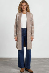 Woman wearing a long beige coat, white top, blue jeans, and brown shoes on a plain background
