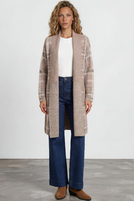 Woman wearing a long beige coat, white top, blue jeans, and brown shoes on a plain background