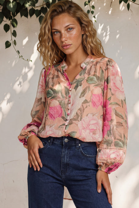Woman wearing a floral blouse and blue jeans against a white wall with greenery.