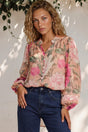 Woman wearing a floral blouse and blue jeans against a white wall with greenery.