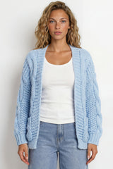 Woman wearing a light blue cardigan over a white top and jeans against a white background