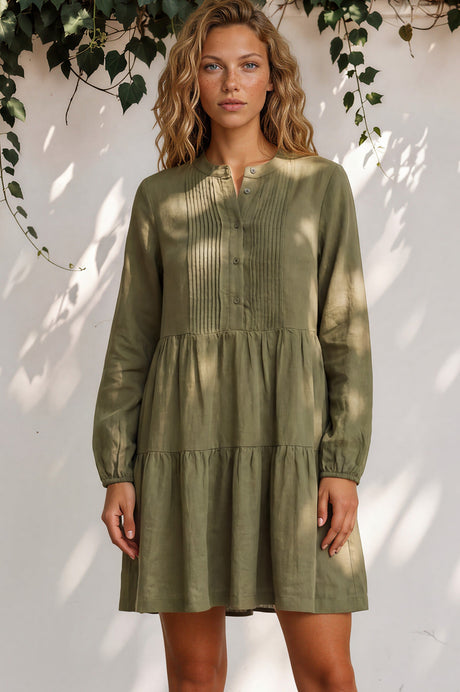 Woman wearing a green dress standing against a white wall with leafy branches.