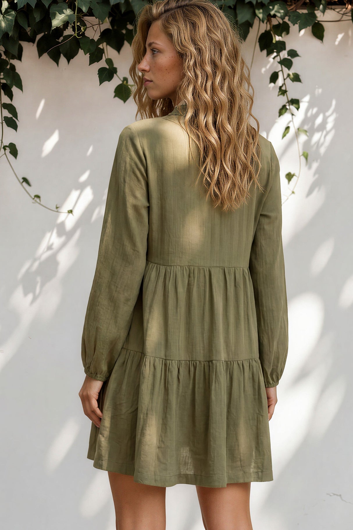 Woman wearing a green dress standing against a white wall with greenery.