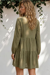 Woman wearing a green dress standing against a white wall with greenery.