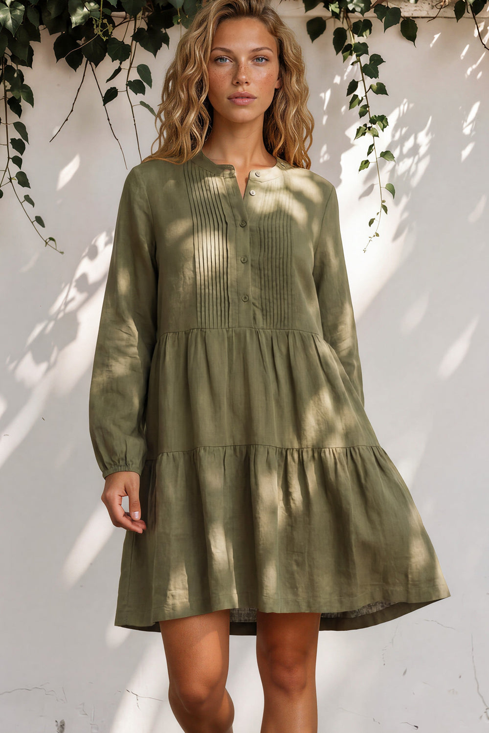 Woman wearing a green dress standing against a white wall with leaves.