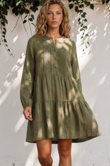 Woman wearing a green dress standing against a white wall with leaves.