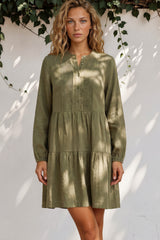 Woman wearing a green dress standing against a white wall with greenery.