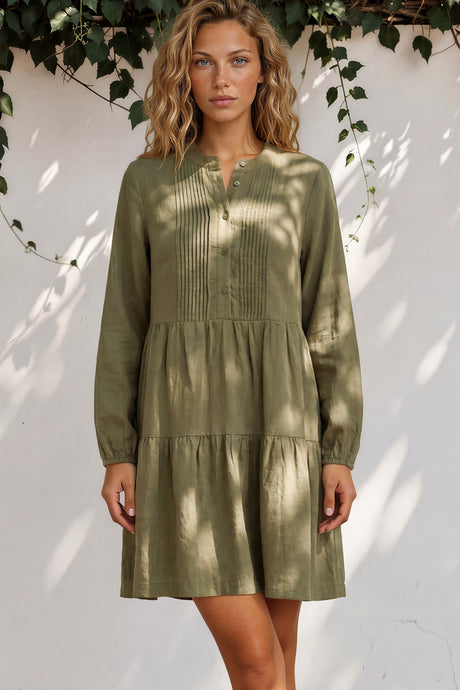 Woman wearing a green dress standing against a white wall with greenery.
