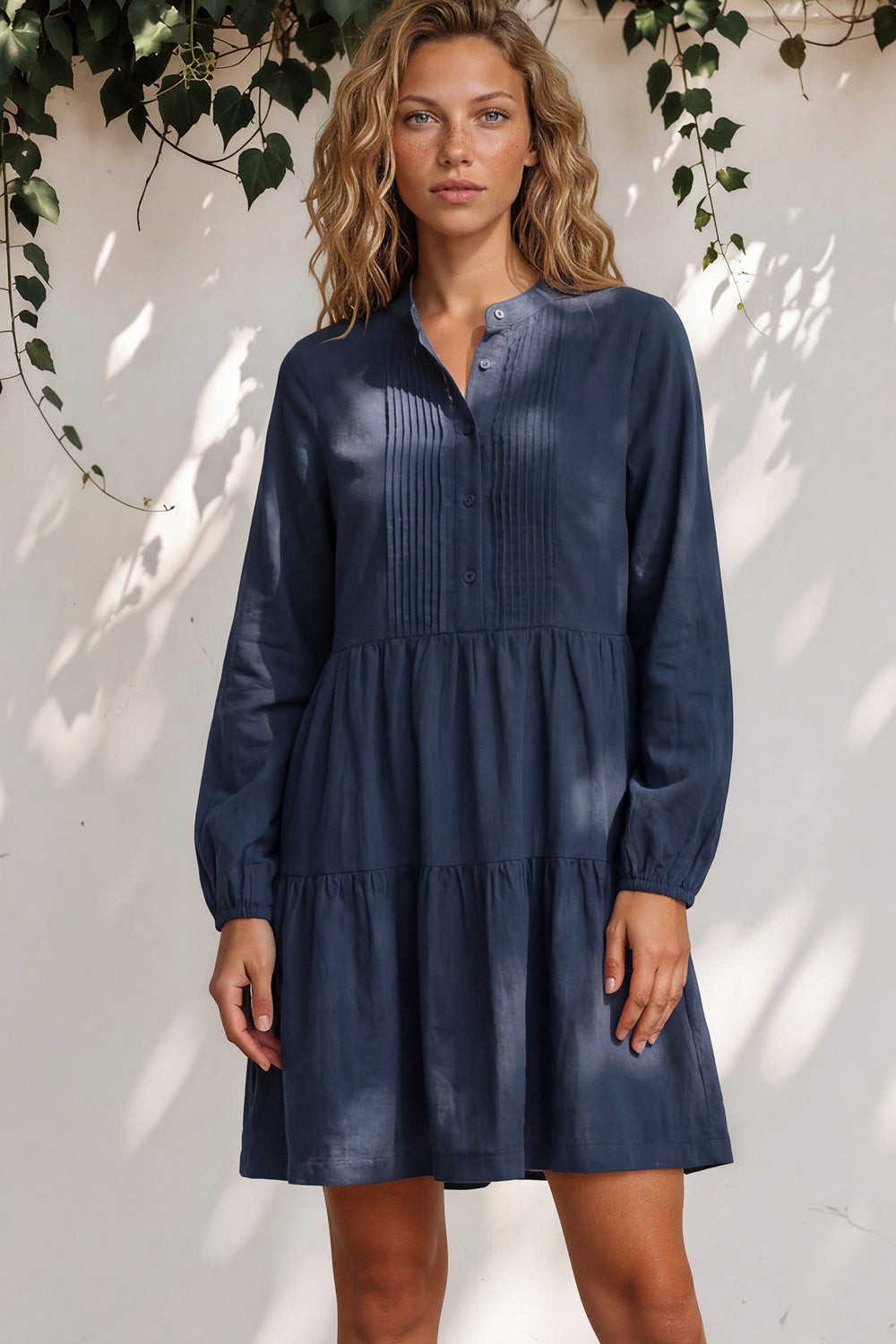 Woman wearing a navy blue dress standing against a white wall with greenery.