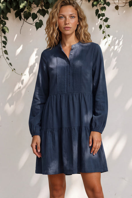 Woman wearing a navy blue dress standing against a white wall with greenery.
