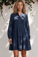 Woman wearing a blue dress standing against a white wall with greenery.