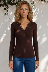 Woman wearing a brown ribbed sweater with button details against a light background