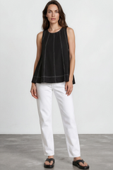 Woman wearing a black sleeveless top and white pants standing against a plain white background