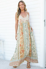 A smiling woman mid-step in the Georgette Maxi Dress in Lyla Print, showing the swishy floor-length skirt with a peach and sage floral stripe print and border hem, against a white wall