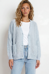 Woman wearing a light blue cardigan over a white shirt and jeans on a plain background
