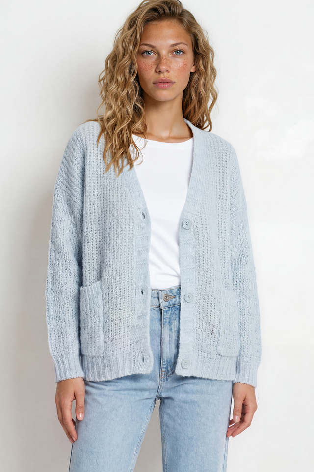 Woman wearing a light blue cardigan over a white shirt and jeans on a plain background