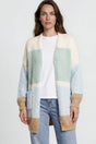Woman wearing a colorful cardigan, white shirt, blue jeans, and white sneakers on a plain background