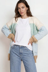 Woman wearing a light blue and beige cardigan over a white shirt and blue jeans on a plain background