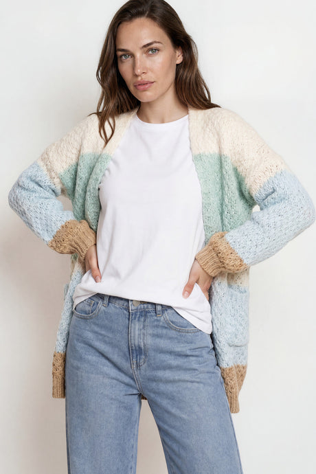 Woman wearing a light blue and beige cardigan over a white shirt and blue jeans on a plain background