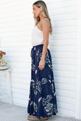 Side view of a woman wearing the Hellen Maxi Skirt in Colette Print, showing the drawstring tie waist and floor-length tiered silhouette of the navy floral skirt, with a white cami against a white wall