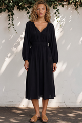Woman wearing a black dress standing against a white wall with greenery.