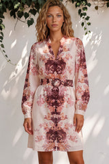 Woman wearing a floral dress standing against a white wall with greenery.