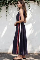 Woman wearing a long dark dress with colorful side panels against a white wall with greenery.