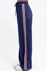Navy blue track pants with red and white stripes on a white background