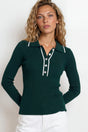 Woman wearing a green long-sleeve polo shirt with white buttons against a plain background