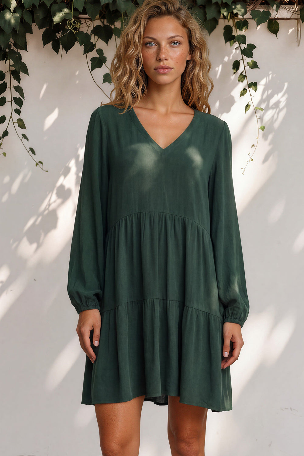 Woman wearing a green dress standing against a white wall with greenery.