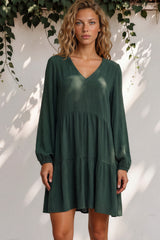 Woman wearing a green dress standing against a white wall with greenery.