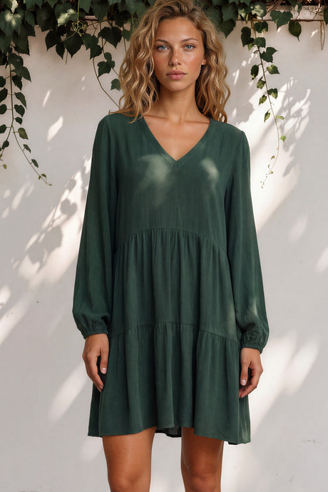 Woman wearing a green dress standing against a white wall with greenery.