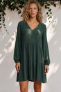Woman wearing a green dress standing against a white wall with greenery.