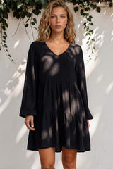 Woman wearing a black dress standing against a white wall with greenery.