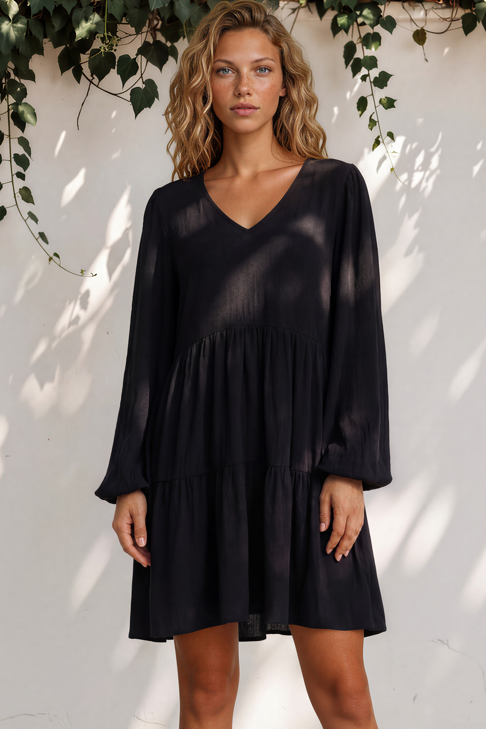 Woman wearing a black dress standing against a white wall with greenery.